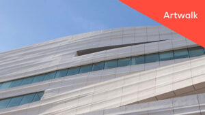 A low-angle shot of the partial exterior of the SFMOMA building with the text "Artwalk" in a red triangle at the top right corner of the image.