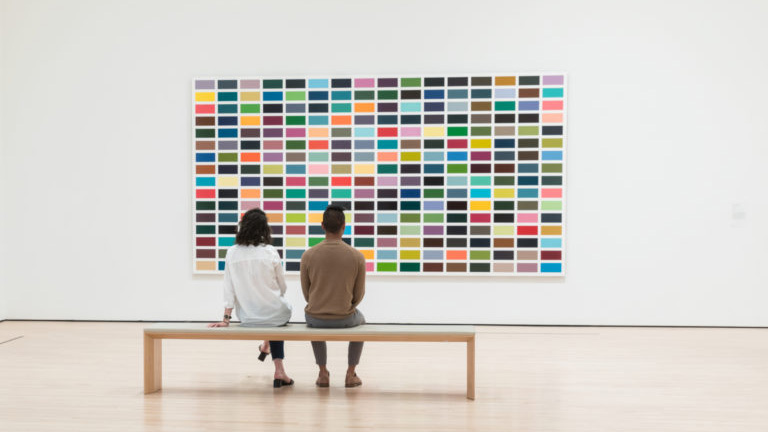Two people sit on a bench observing Gerhard Richter's artwork 256 Farben (256 Colors) in the SFMOMA gallery for German art.
