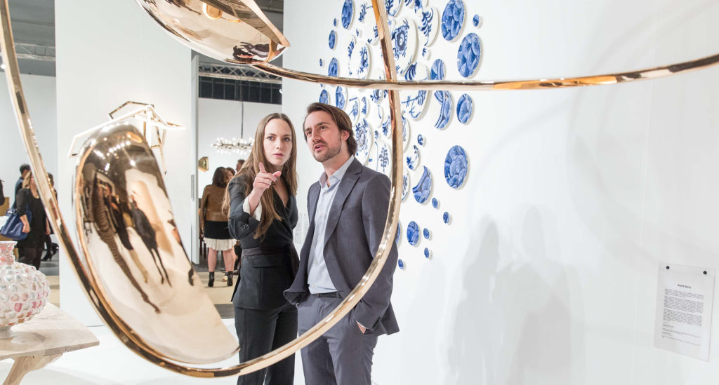 A man and woman at an art event pointing at a large gold sculpture