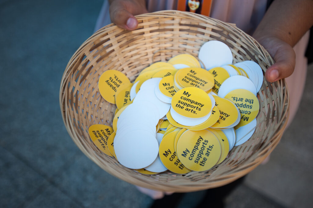 A basket of stickers reading "My organization supports the arts."
