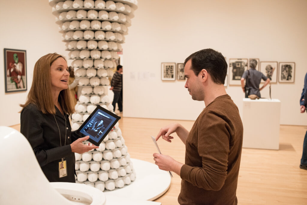 A docent with an iPad talks to a man in a gallery in front of a large sculpture
