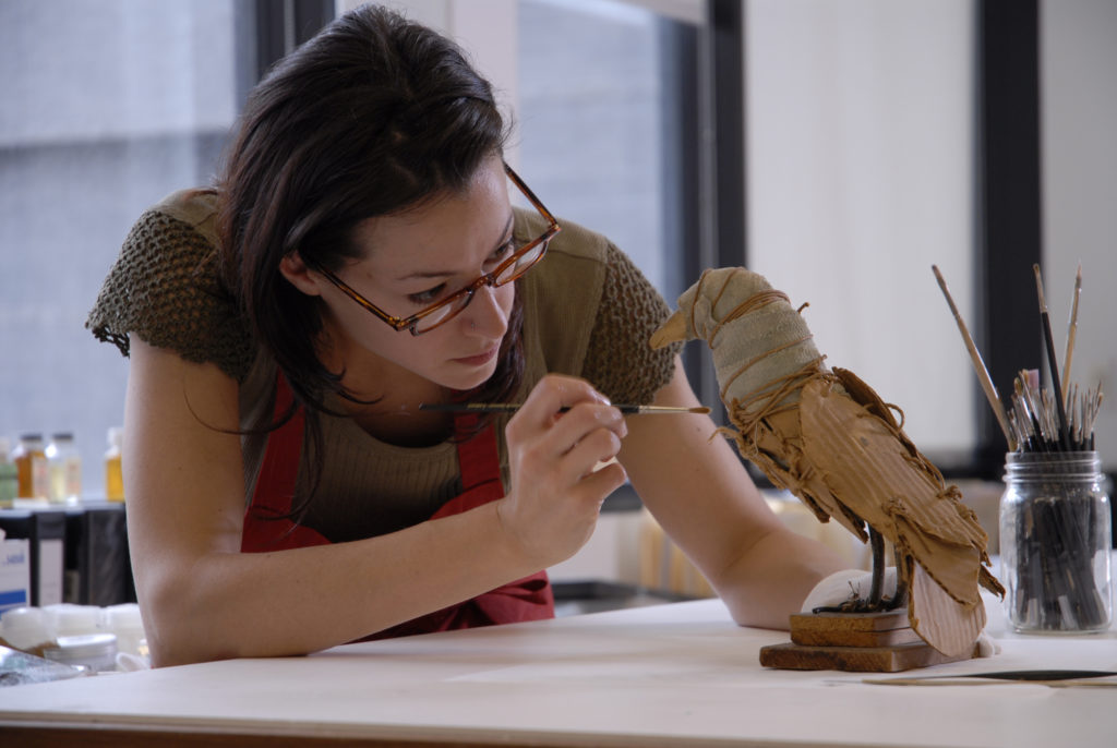 A conservator working on a bird sculpture with a paintbrush