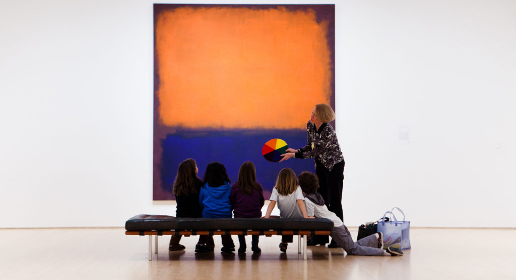 A group of students and a teacher in front of a large blue and orange abstract painting