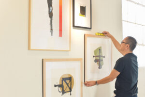 A man placing framed paintings on a wall