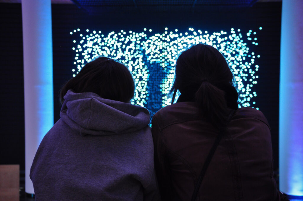 Two seated women in silhouette looking at an uneven grid of bright lights