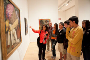 A guide explains a Diego Rivera painting to a group of students