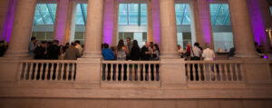A group of people mingle and eat on a museum balcony