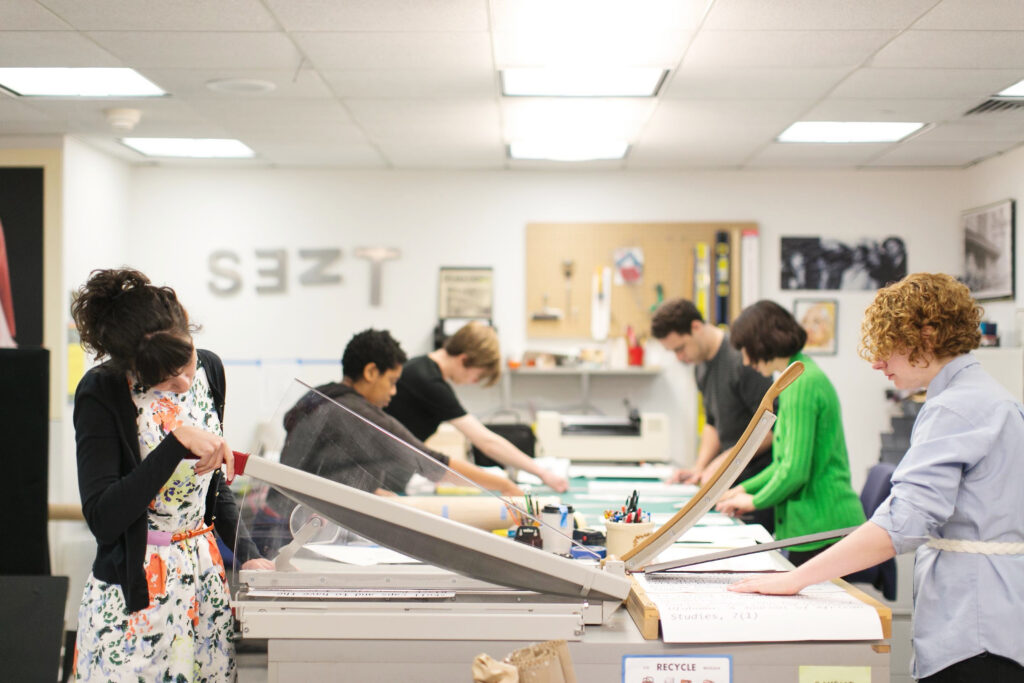 Six people work at a long drafting table
