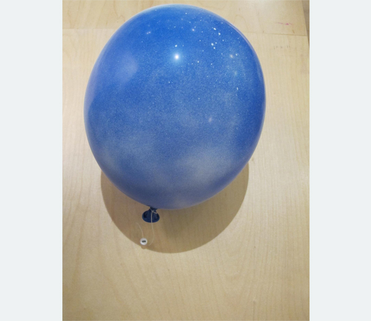 A blue balloon is tied to a tack on a wood suface with a short piece of white string