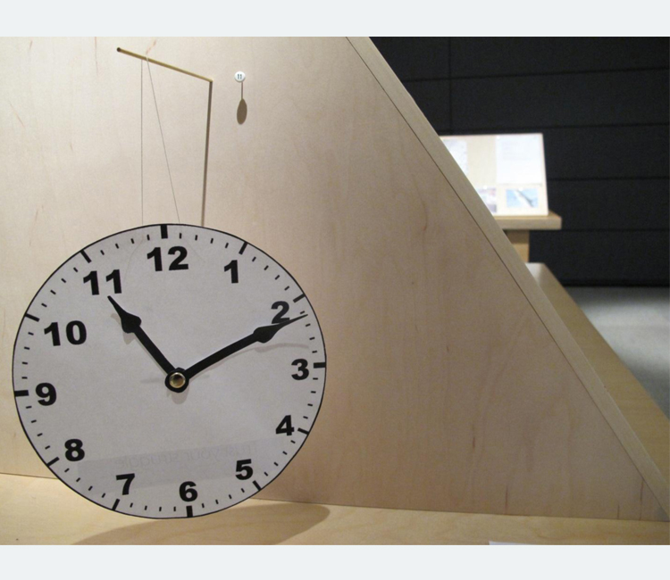 A round white paper clock with black hands and numbers hangs from a wooden partition