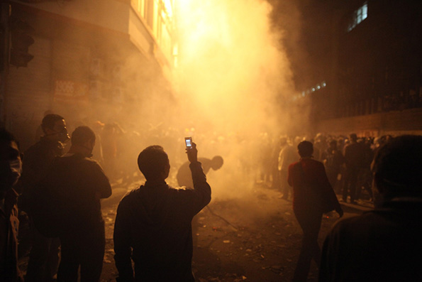 Protestors in a smokey street film on cell phones