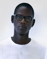 A man with glasses stands in front of a white wall