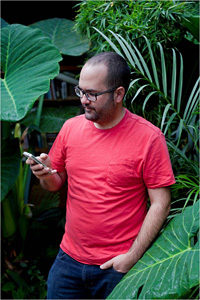 A man stands among tropical plants and looks at his phone