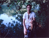 A man poses under a tree by a pond