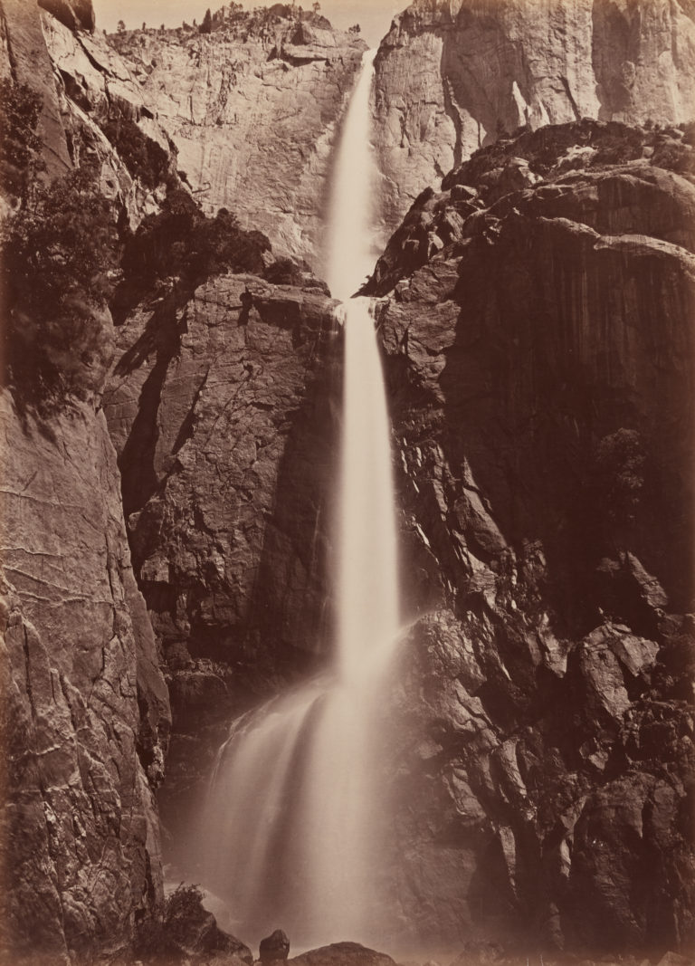 Sepia-toned black and white photograph of a tall cascading waterfall seen from below 
