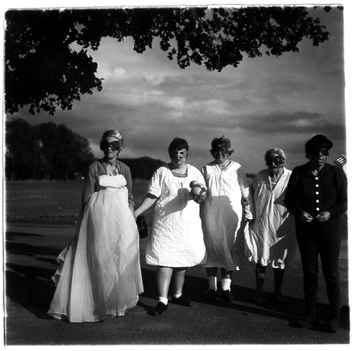 Black and white photograph of five masked people of various ages standing beneath a tree on a large, open lawn