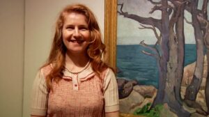 A smiling woman stands in front of a framed painting