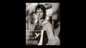 A black and white photograph of a young woman holding a sign reading "War is not the answer!'