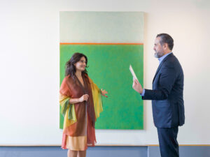 Two people speaking in front of a green, white, and orange painting
