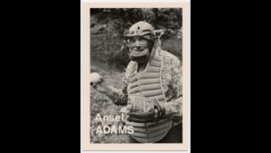 Photograher Ansel Adams wearing a baseball glove and mask, posing with a baseball as if on a baseball card.