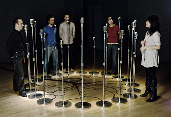 five people standing around circle of microphones