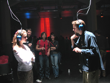 Gommel, installation view of woman and man looking at each other wearing headphones