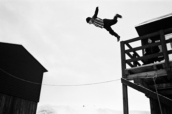 black and white photo man jumping off building onto tight rope