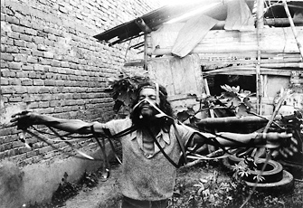 Carlos Mayolo and Luis Ospina, photo of man covered in straps with arms up in front of hut