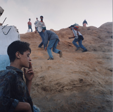 Yto Barrada, men climbing rock crossing border with young boy in foreground