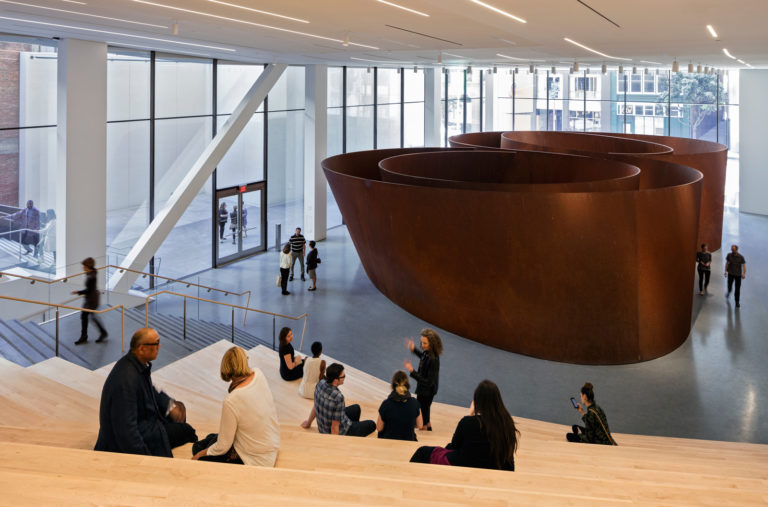 Visitors sit on steps before a massive spiraling bronze sculpture
