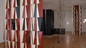 A room full of sculptural art made of rope, large pieces of hanging leather, and screens made of long red, white and red metal triangles.