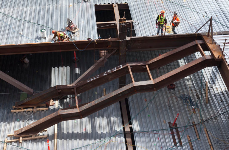 Steel beams form the beginnings of a staircase with construction workers wearing hardhats