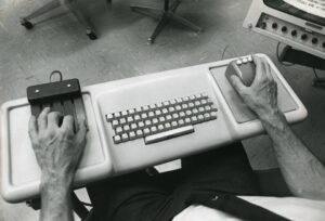 Two disembodied arms set on a white keyboard holding two old computer mice; Typeface to Interface