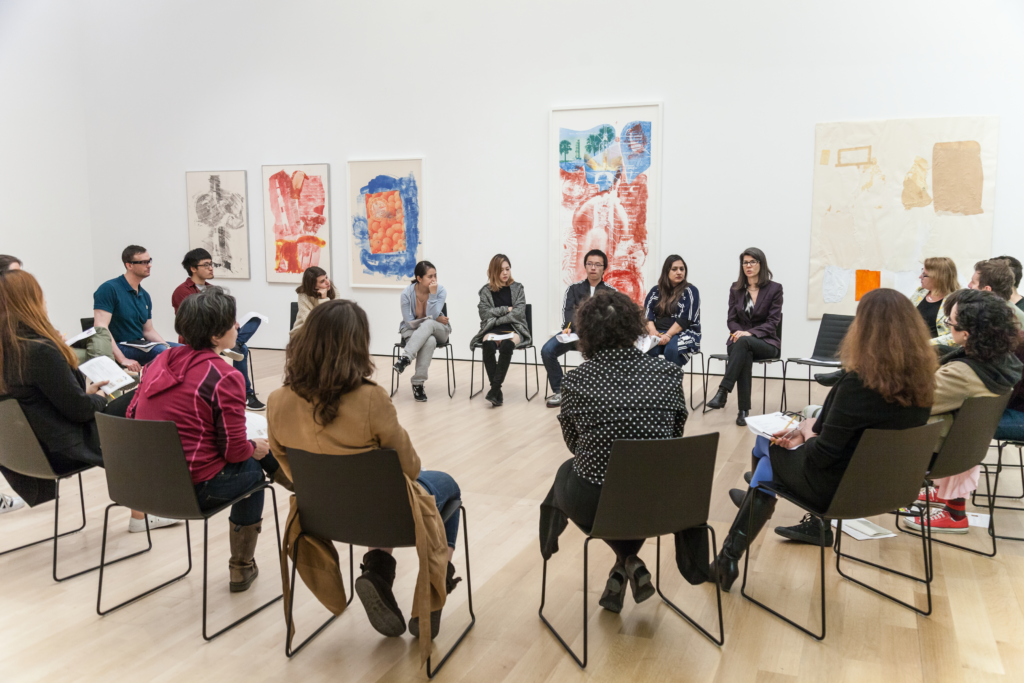 A group od people sit in chairs in a circle in a gallery