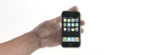 A hand holds an first generation iPhone against a white background