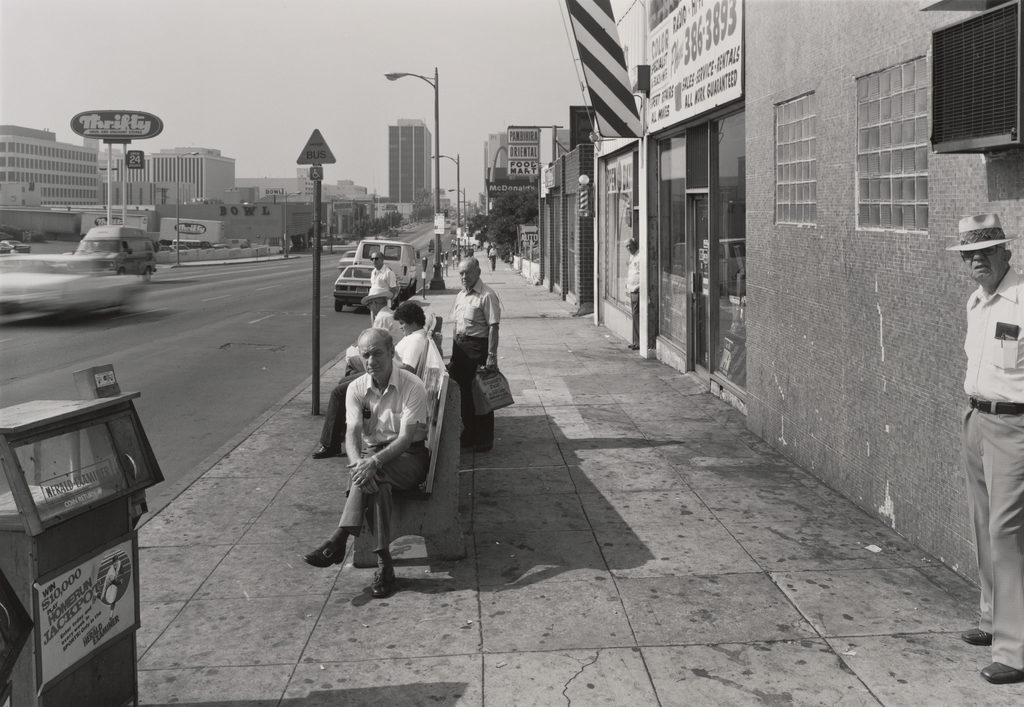A black and white photograph of people sitting at a bus stop