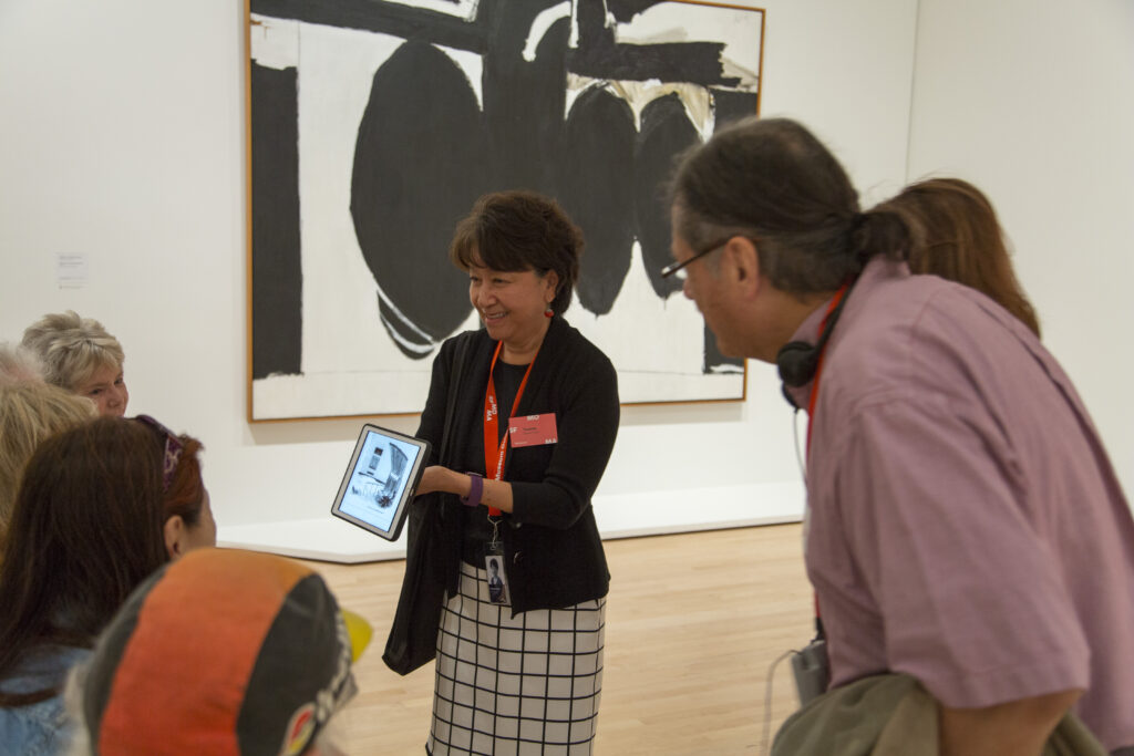 A museum guide shows a New Yorker cartoon on an iPad in a gallery