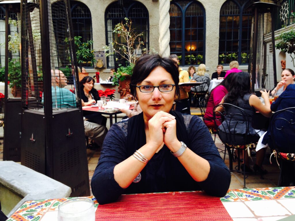 A woman with glasses sits at a table in a courtyard
