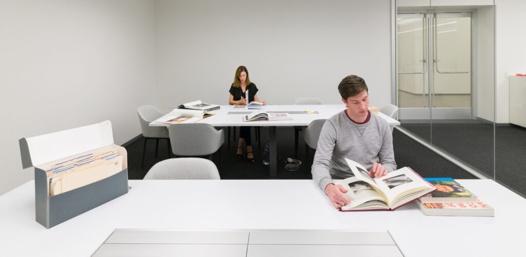 Two people sit in a white room looking at books