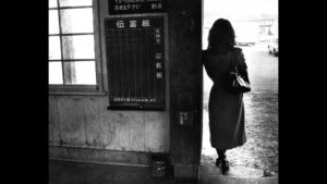 A black and white photograph showing a woman in 1940's Japan, standing in a doorway with her back to the camera