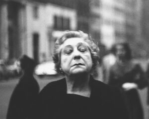 A photograph of a woman on the street with her eyes closed