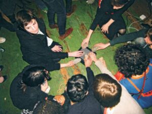 A group of people sit in a circle with their hands together in the center