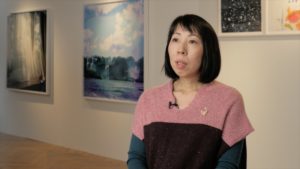 Photographer Rinko Kawauchi sitting in a gallery with colorful photographs behind her