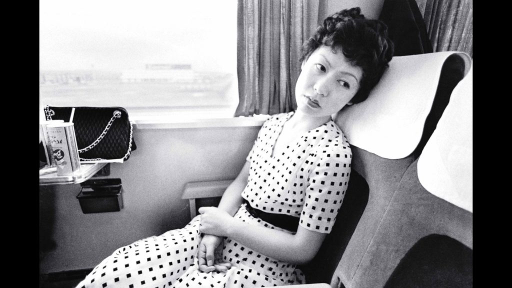 A black-and-white photograph of a glamorous, dejected-looking woman on a train
