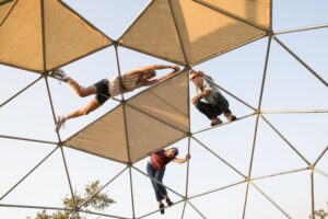 Three people seen from below climb on a geodesic dome