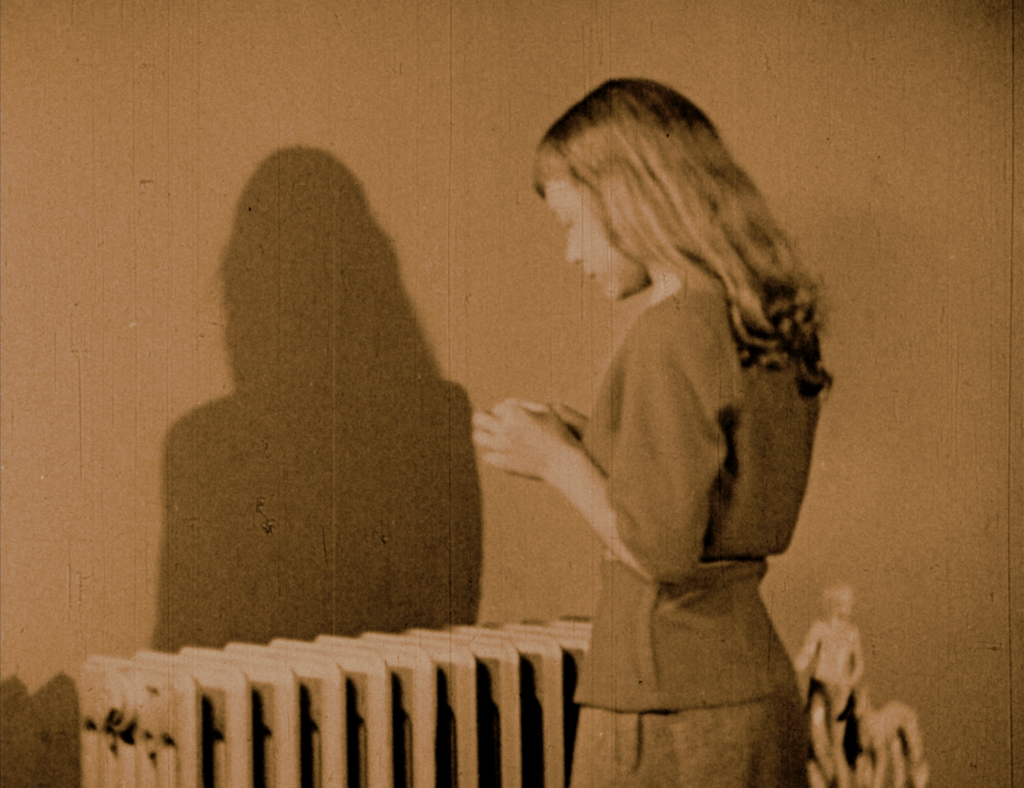 A film still picturing a woman with long blond hair with her back turned