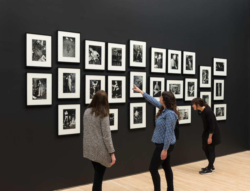 Three women look at a wall of Bruce Conner's punk photographs