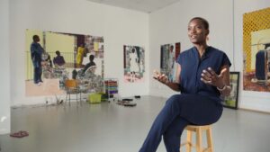 Artist Njideka Akunyili Crosby in her studio, with several large figurative paintings on the walls behind her
