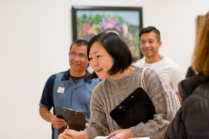 A smiling woman looks intently at something out of the frame in a gallery