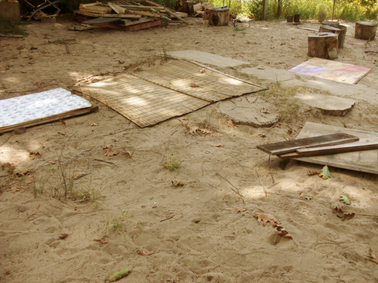 A photograph of a woven mat, plywood, and cement block lined up over an expanse of sand